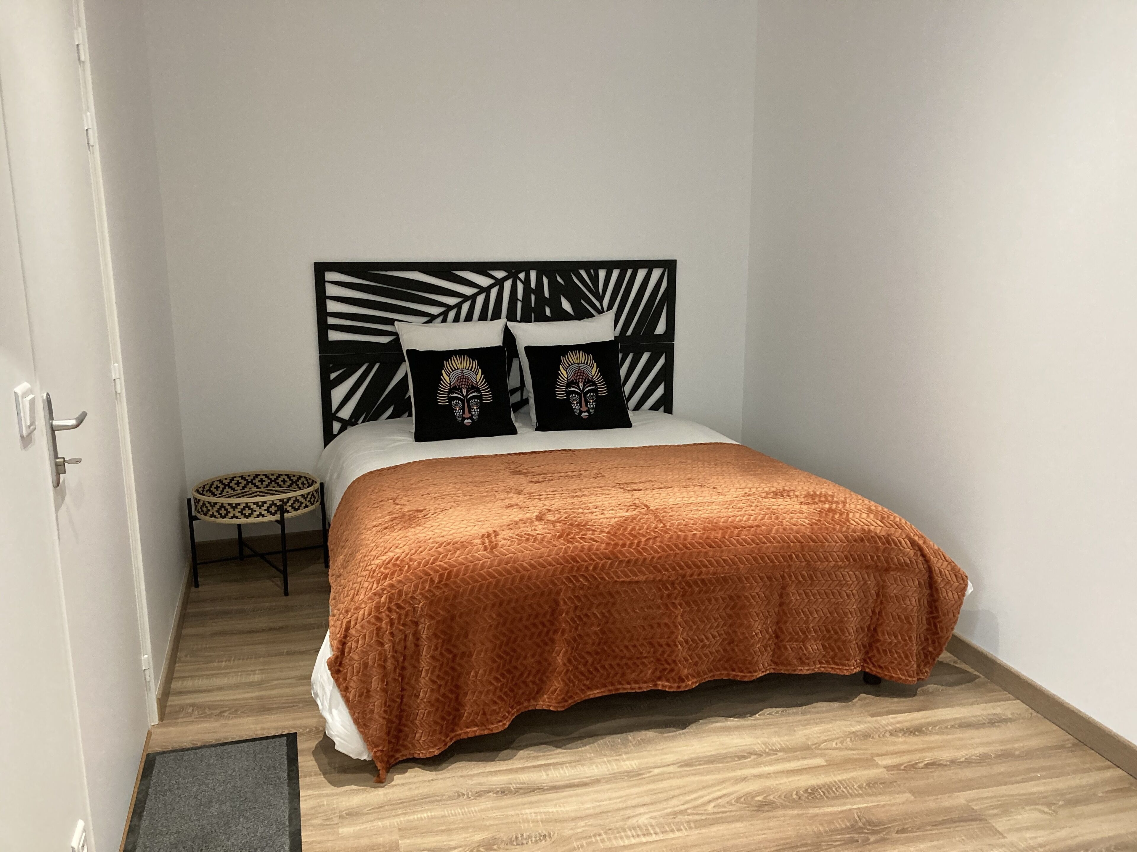 Un dormitorio con cama, cabecera estampada con motivos florales, mesita redonda y alfombra con diseño.