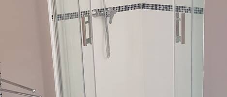 Una ducha con paredes de vidrio, un panel de control y un banco acolchado rojo en primer plano.