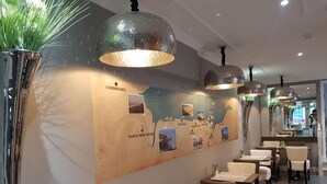 A restaurant with a map on the wall, tables, chairs, and hanging pendant lights. - Hôtel Le St Patrice (Bayeux)