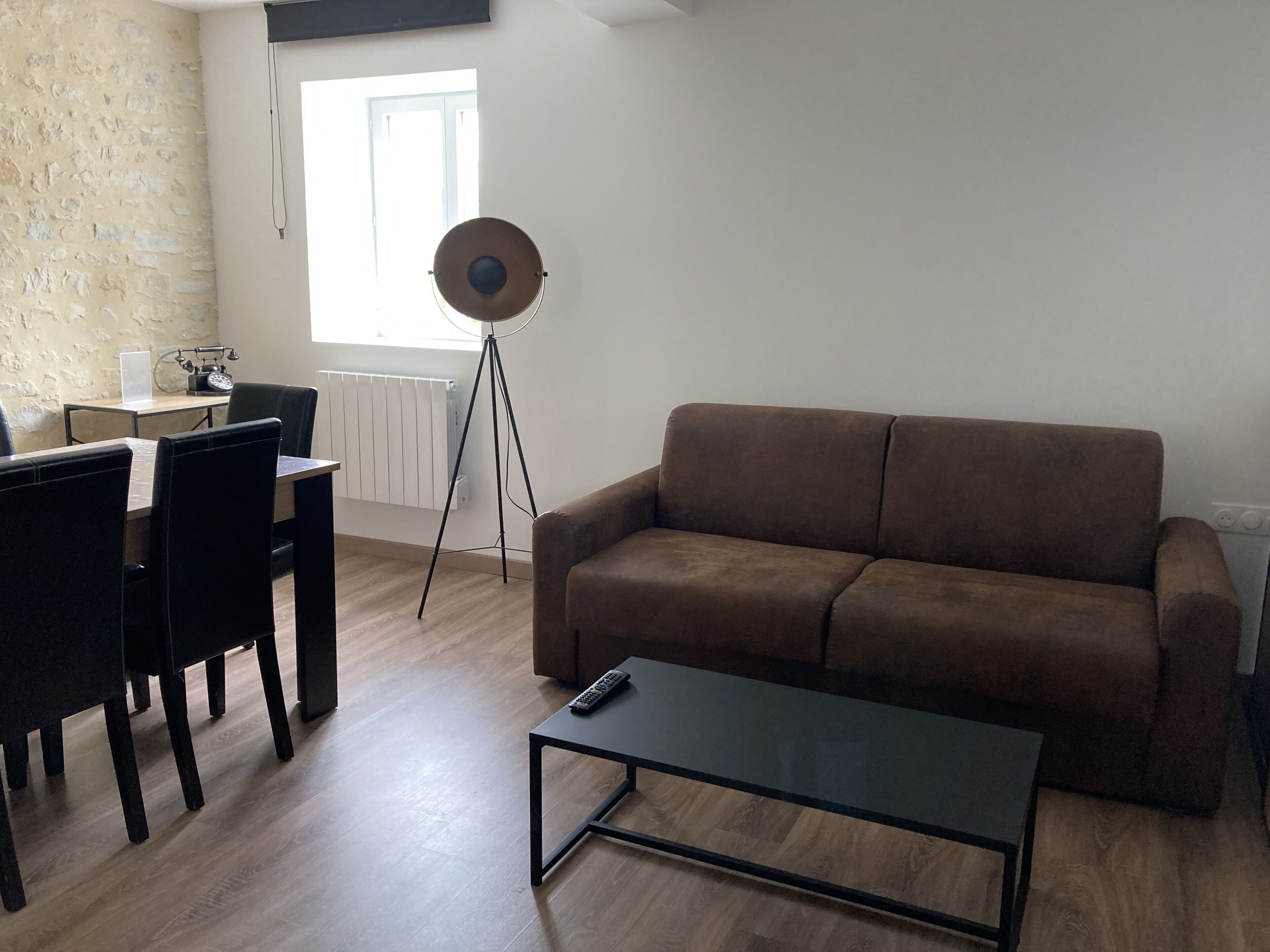 Een woonkamer met een bruine bank, een salontafel en een eethoek met stoelen en een tafel.