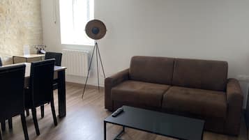 Een woonkamer met een bruine bank, een salontafel en een eethoek met stoelen en een tafel.