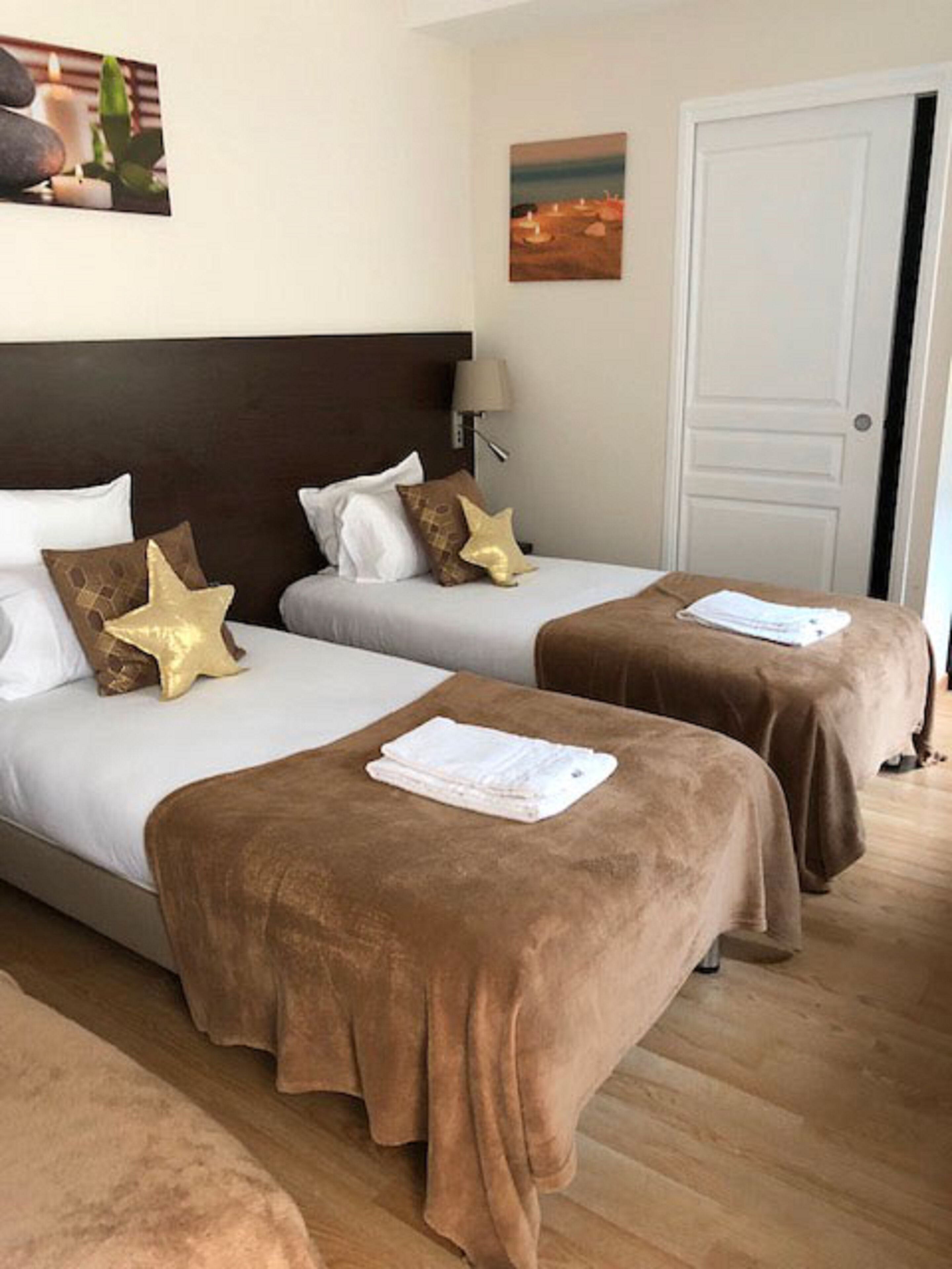 Ein Hotelzimmer mit zwei Betten, jeweils mit brauner Bettdecke und Kissen, einem Nachttisch mit Lampe und einer Tür.