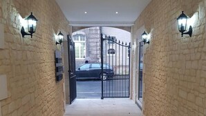 A hallway with stone walls, a tiled floor, and a gated entrance with a car parked outside. - Hôtel Le St Patrice (Bayeux)