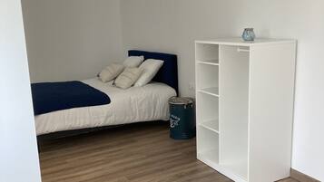 A bedroom with a bed, a white wardrobe, and a blue trash bin.