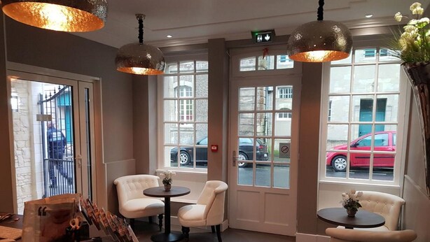 A modern interior with two round tables and four white chairs, large windows with a view of the street, and pendant lighting. - Hôtel Le St Patrice (Bayeux)