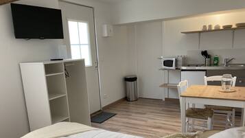 A compact room with a bed, a small kitchenette, a TV mounted on the wall, and a window.