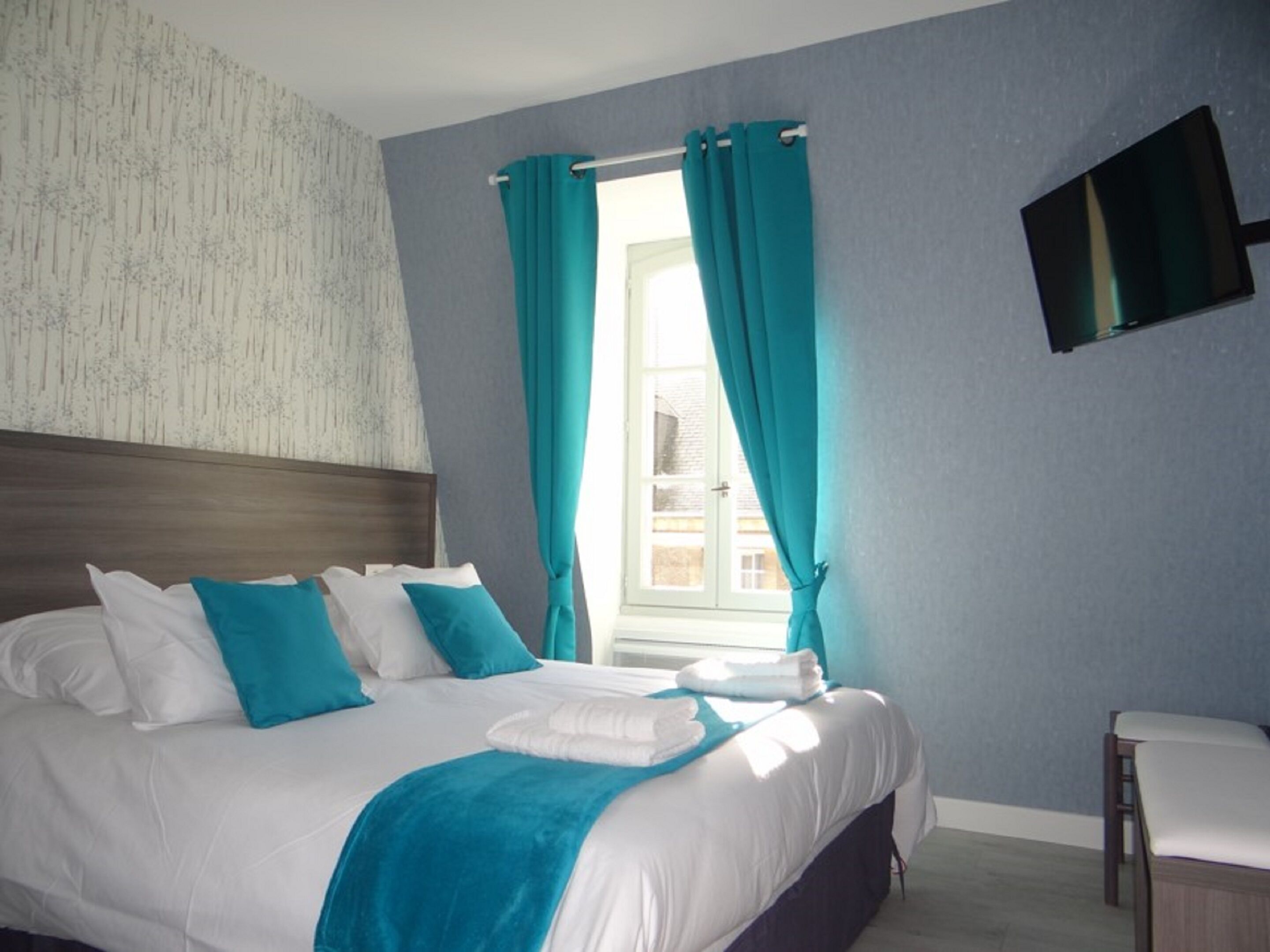Habitación de hotel moderna con una cama grande, cortinas color turquesa, un televisor de pantalla plana y vistas a la ciudad.