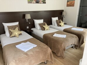 A hotel room with two beds, each with a brown blanket and white linens. There are star-shaped pillows on the beds, and a nightstand with a lamp between them. - Hôtel Le St Patrice (Bayeux)