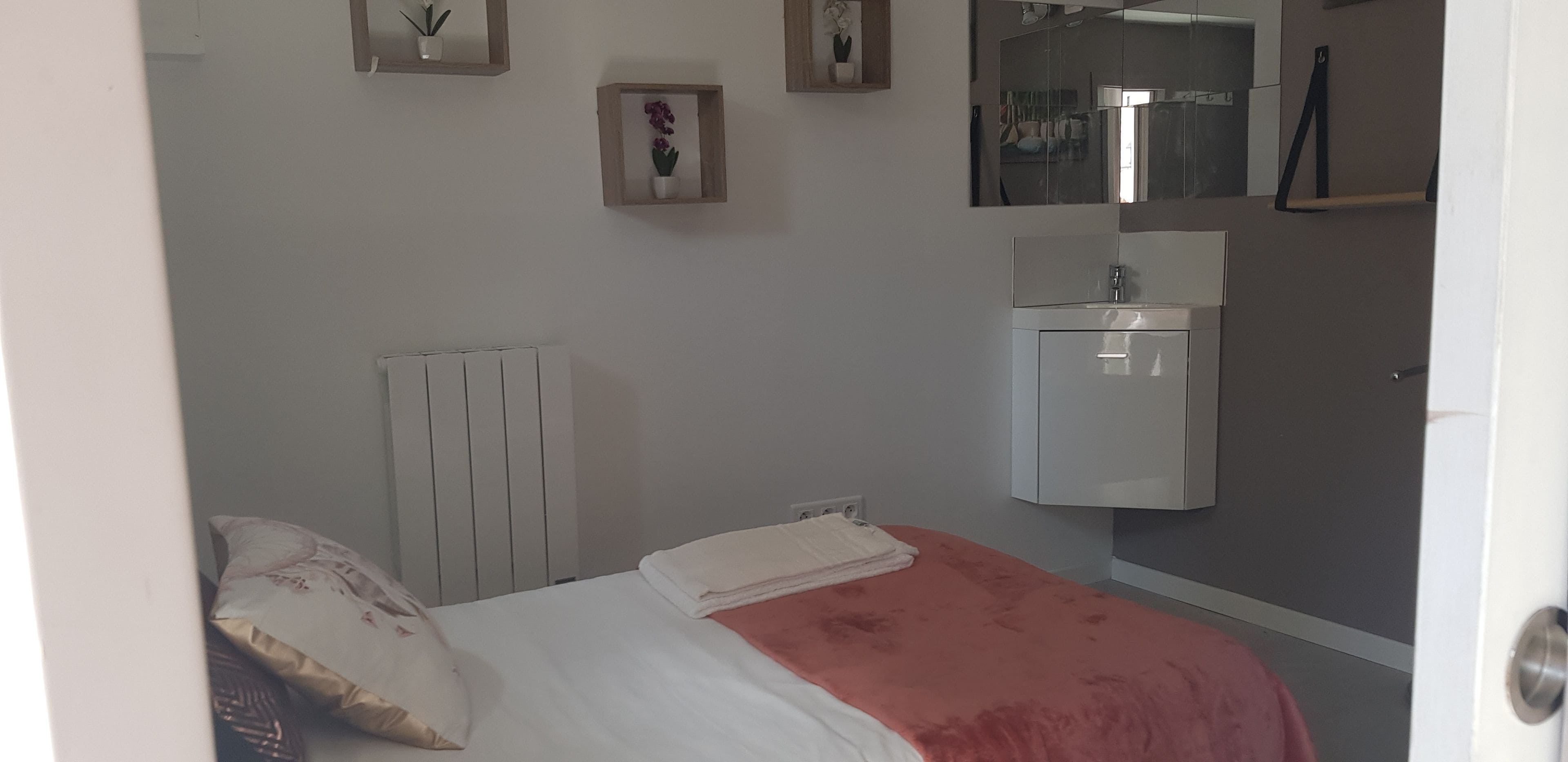 Une chambre à coucher avec un lit, un radiateur, une petite armoire et un miroir au mur.
