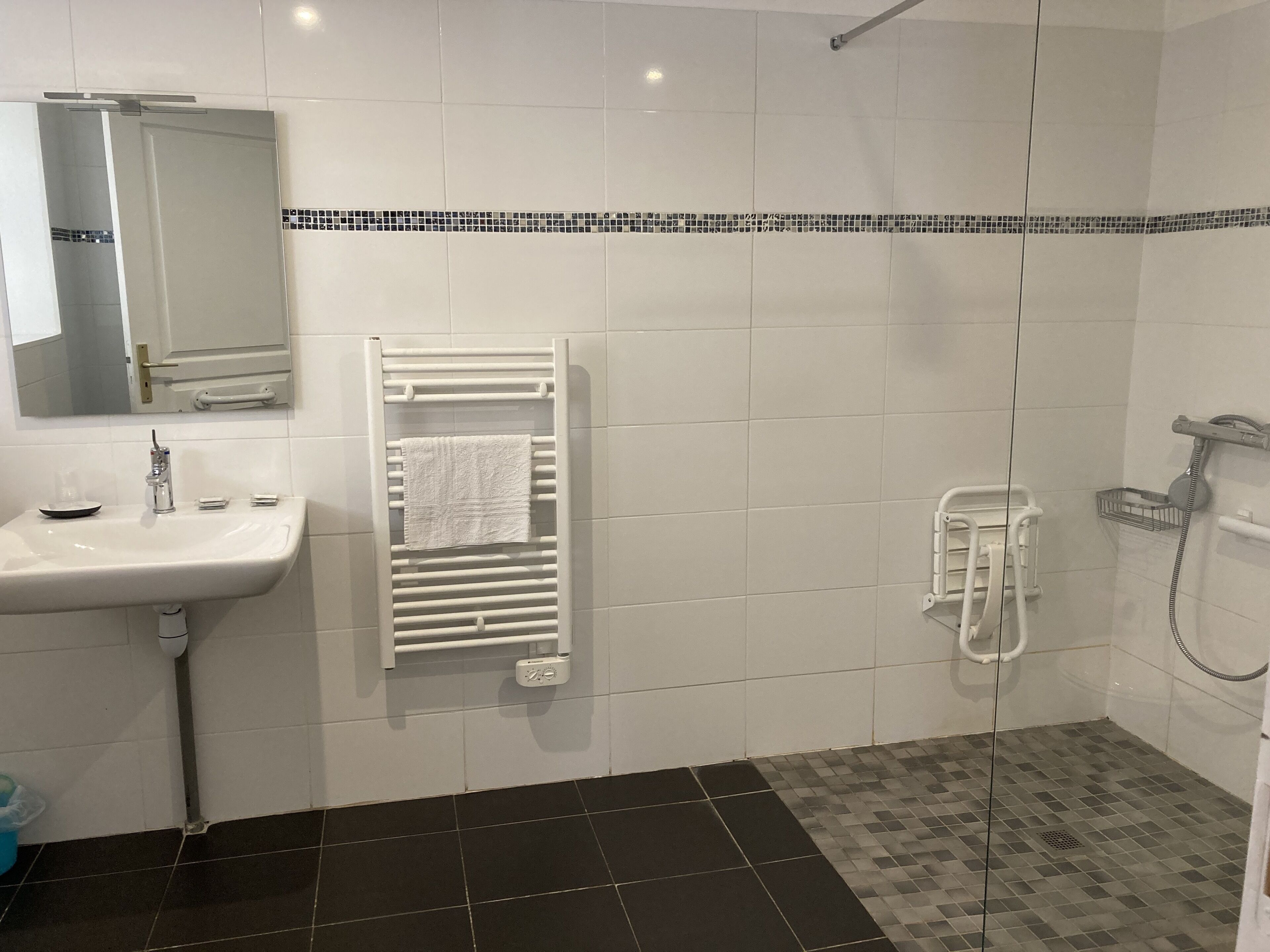 Een badkamer met een wastafel, spiegel, handdoekhouder, douche en betegelde vloer.