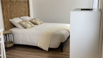 Un dormitorio con cama, una mesita, una silla, un armario blanco y una viga de techo de madera.