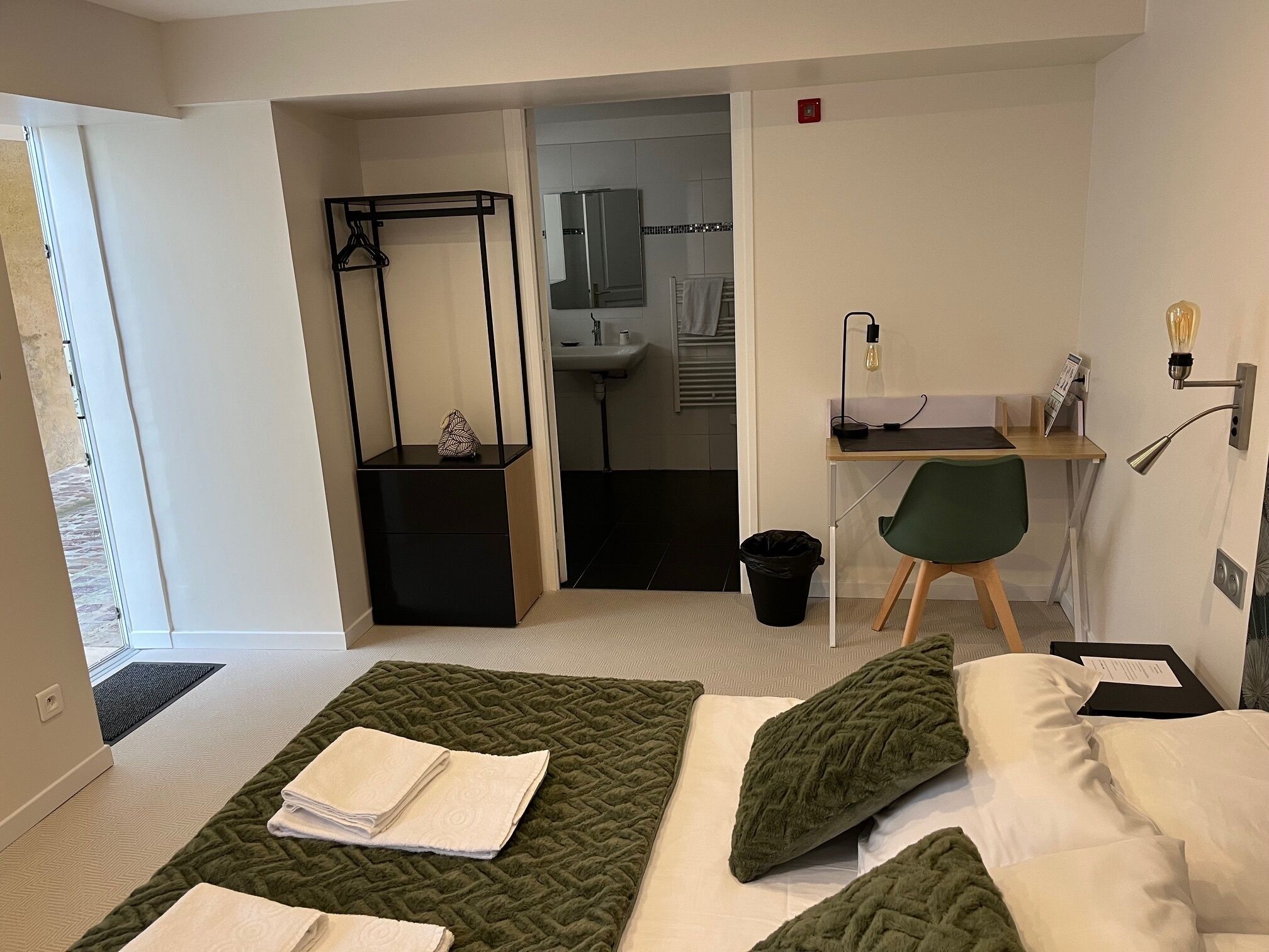 Une chambre d’hôtel équipée d’un lit, d’un bureau, d’une chaise, d’un porte-manteau et d’une petite poubelle.
