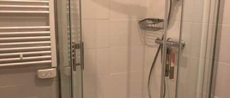 Una ducha con cerramiento de vidrio, cabezal de ducha de mano y grifo empotrado.