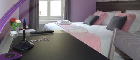Une chambre d’hôtel avec un lit, un bureau doté d’une lampe, une télécommande et un vase avec des fleurs.