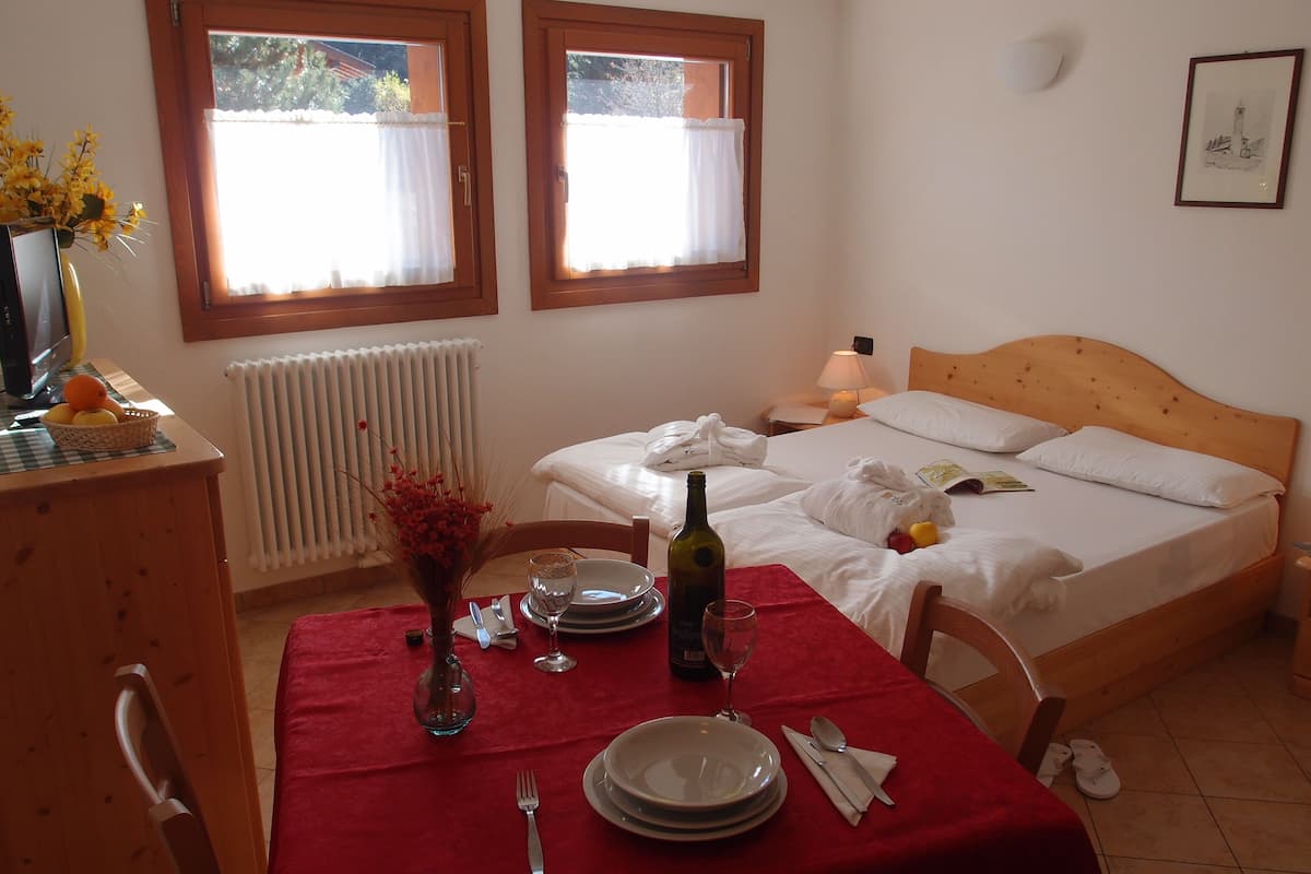A neatly arranged bedroom with a wooden bed, a bedside table with a lamp, and a window with curtains.