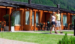 A wooden lodge with a covered patio, outdoor seating, and a view of the forested mountains.