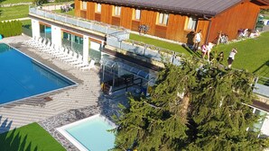 An aerial view of a hotel with a large swimming pool, a smaller pool, and a deck area with lounge chairs. - Dolomiti Camping Village&Wellness Resort (Dimaro Folgarida)