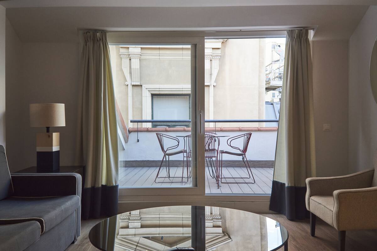 A hotel room with a balcony, a sofa, a table, and a chair.