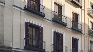 A multi-story building with balconies, red shutters, and a clear sky. - Slow Suites Bellas Artes (Madrid)