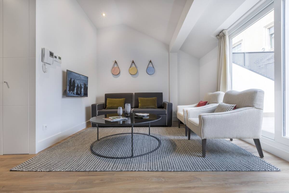 A modern living room with a sofa, armchair, coffee table, and a patterned rug.