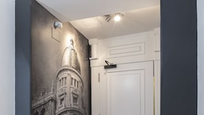 A hallway with a mural of a building, a white door with a gold handle, and a marble floor. - Slow Suites Bellas Artes (Madrid)