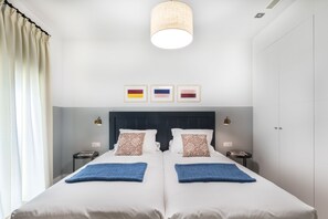 Una cama doble con dos mantas azules, un cabecero oscuro y tres cuadros en la pared.