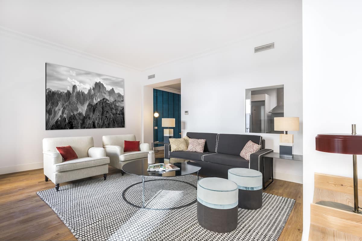 A modern living room with a sofa, armchairs, a coffee table, and a large painting.
