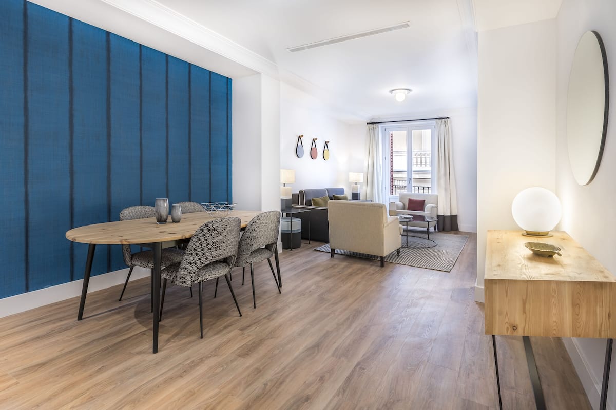 A modern living room with a dining area, featuring a wooden dining table, patterned chairs, a sofa, and a coffee table.