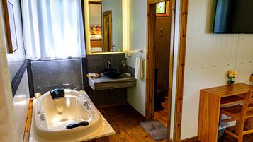 A bathroom with a bathtub, sink, mirror, wooden floor, and a wooden table with a chair.