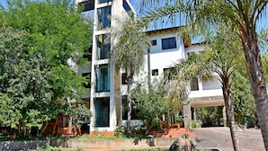Un edificio moderno de varios pisos con piscina, rodeado de exuberante vegetación y palmeras.