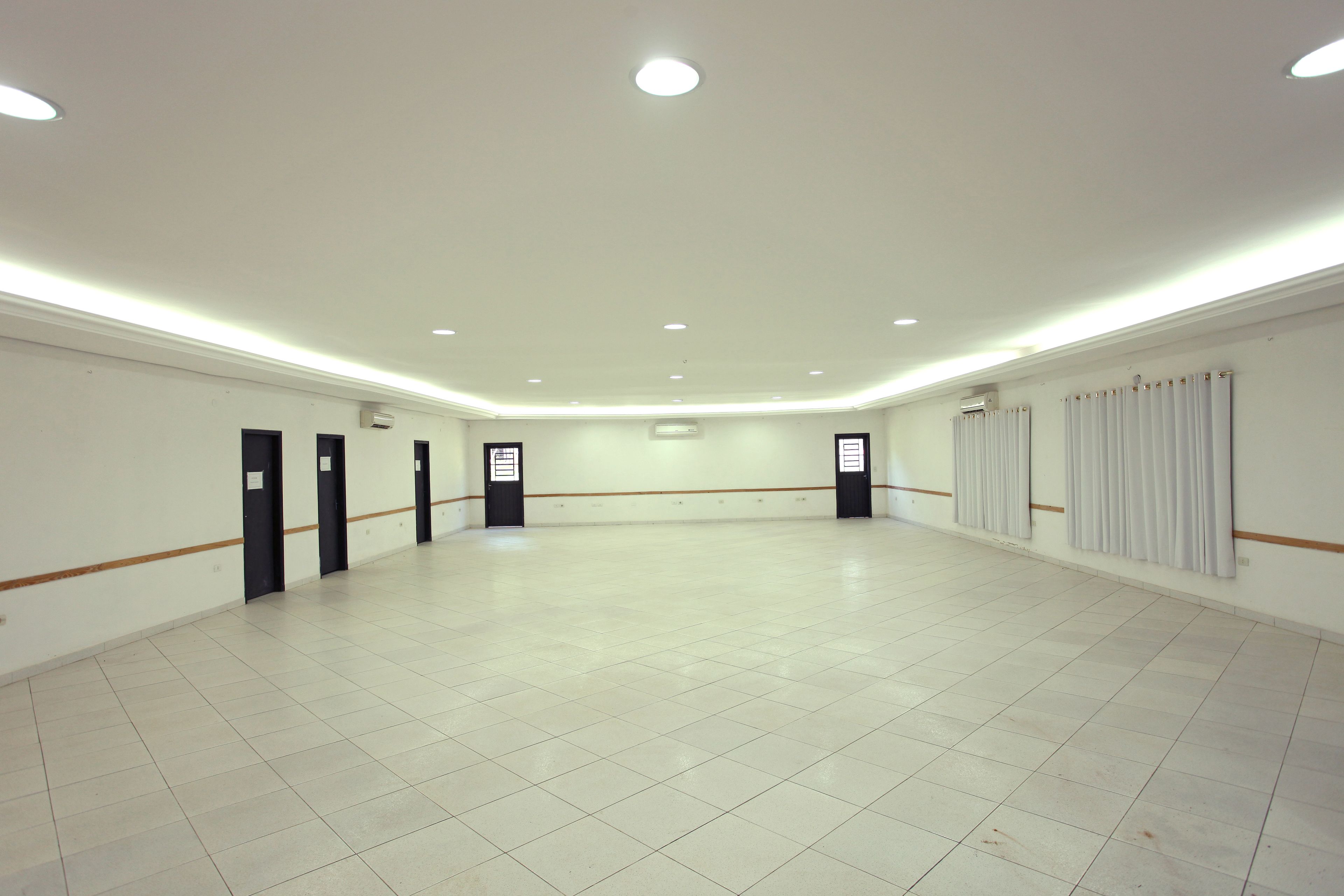 A spacious, well-lit room with a tiled floor, recessed ceiling lights, and a plain white wall.