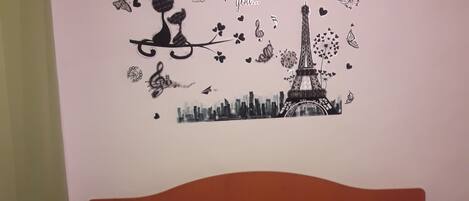 A bedroom with a bed, a headboard, and a wall decoration featuring the Eiffel Tower and musical notes.