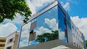 A modern building with a glass facade reflecting the sky and clouds. There are outdoor seating areas with umbrellas and chairs. - Hotel do Mar Cabo Branco (João Pessoa)