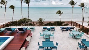An outdoor seating area with tables and chairs, overlooking a beach and the ocean. - Hotel do Mar Cabo Branco (João Pessoa)