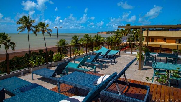A beachside lounge with lounge chairs and tables, palm trees, and a view of the ocean. - Hotel do Mar Cabo Branco (João Pessoa)