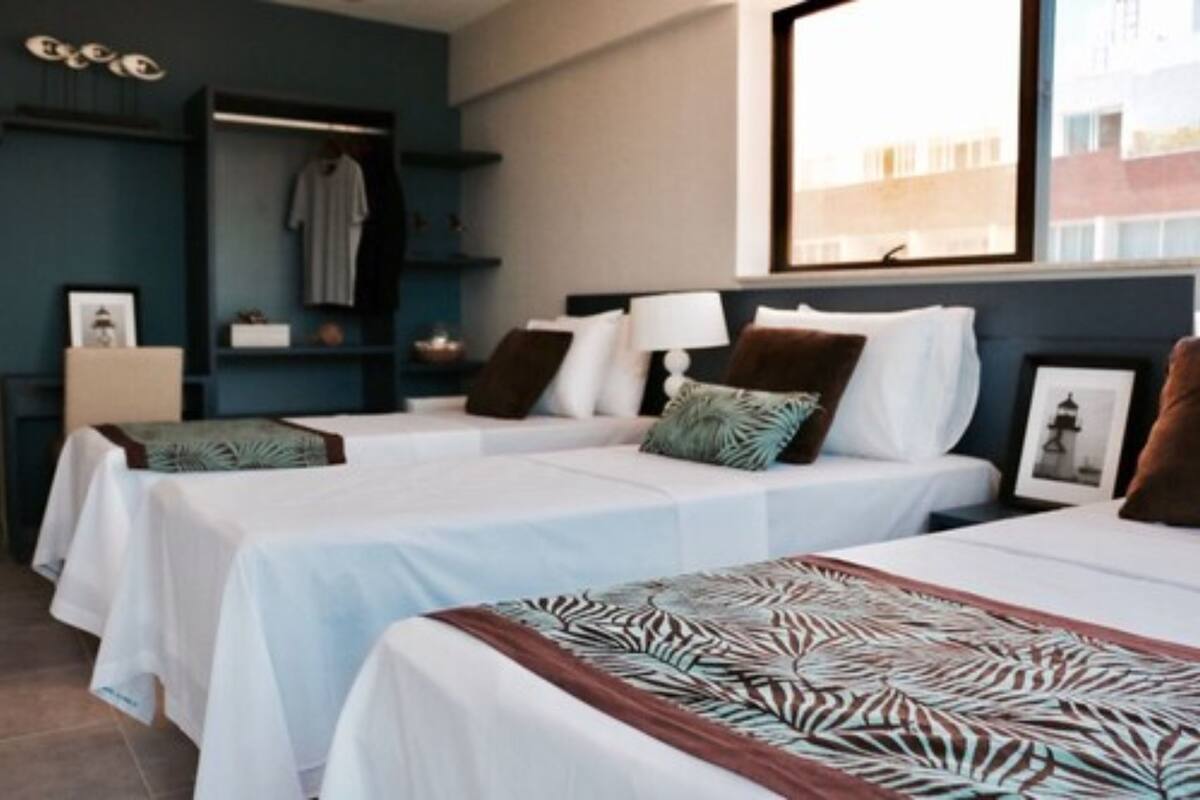 Une chambre d’hôtel avec deux lits, une armoire, une table de chevet et une fenêtre donnant sur des immeubles.