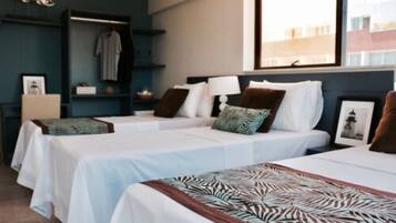 Een hotelkamer met twee bedden, een kledingkast, een nachtkastje en een raam met uitzicht op gebouwen.