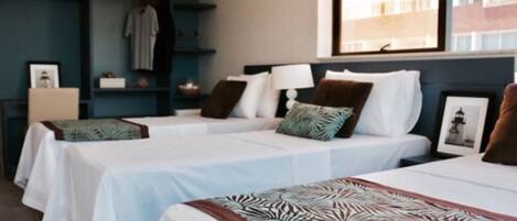 A hotel room with two beds, a wardrobe, a bedside table, and a window with a view of buildings.