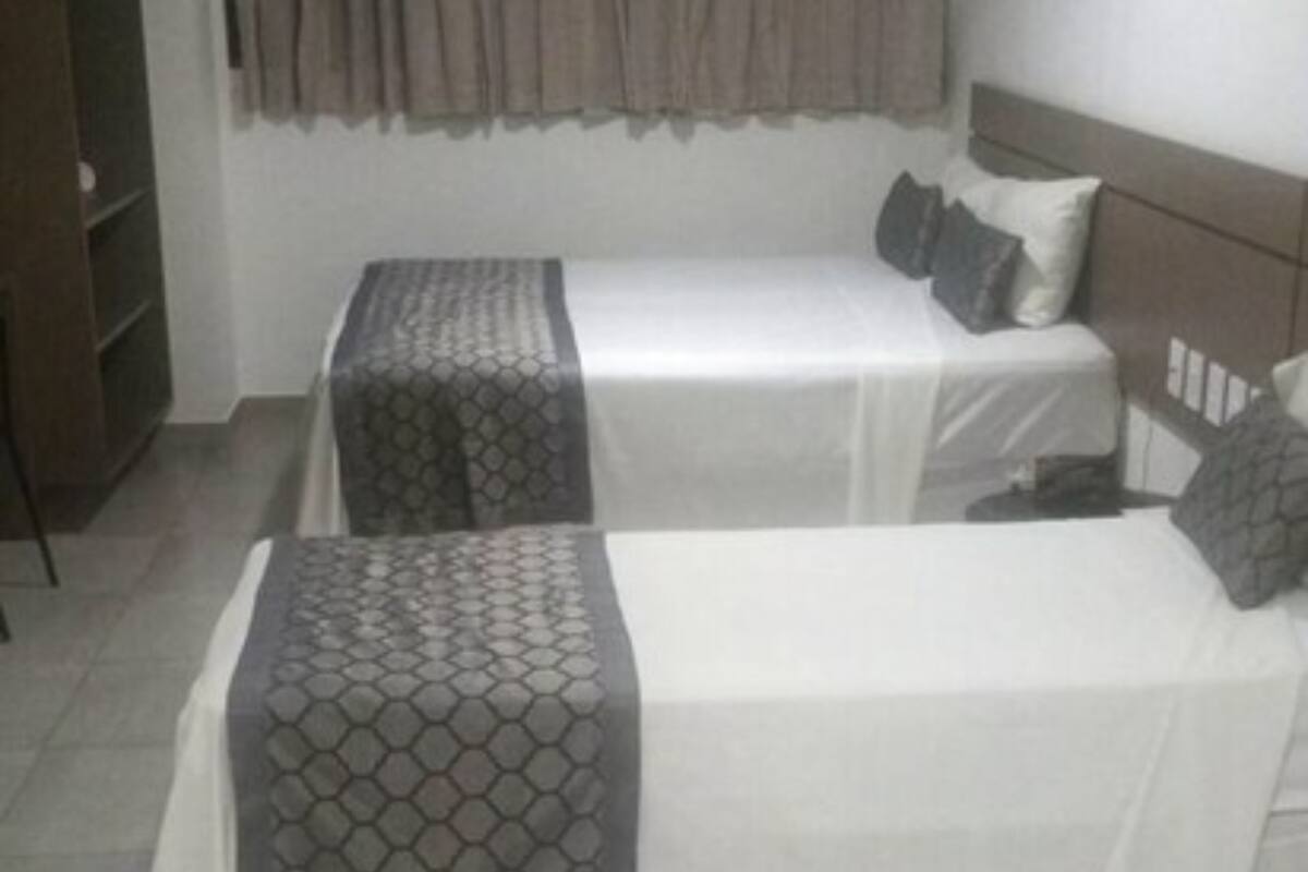 Une chambre avec deux lits simples, une armoire et un rideau.
