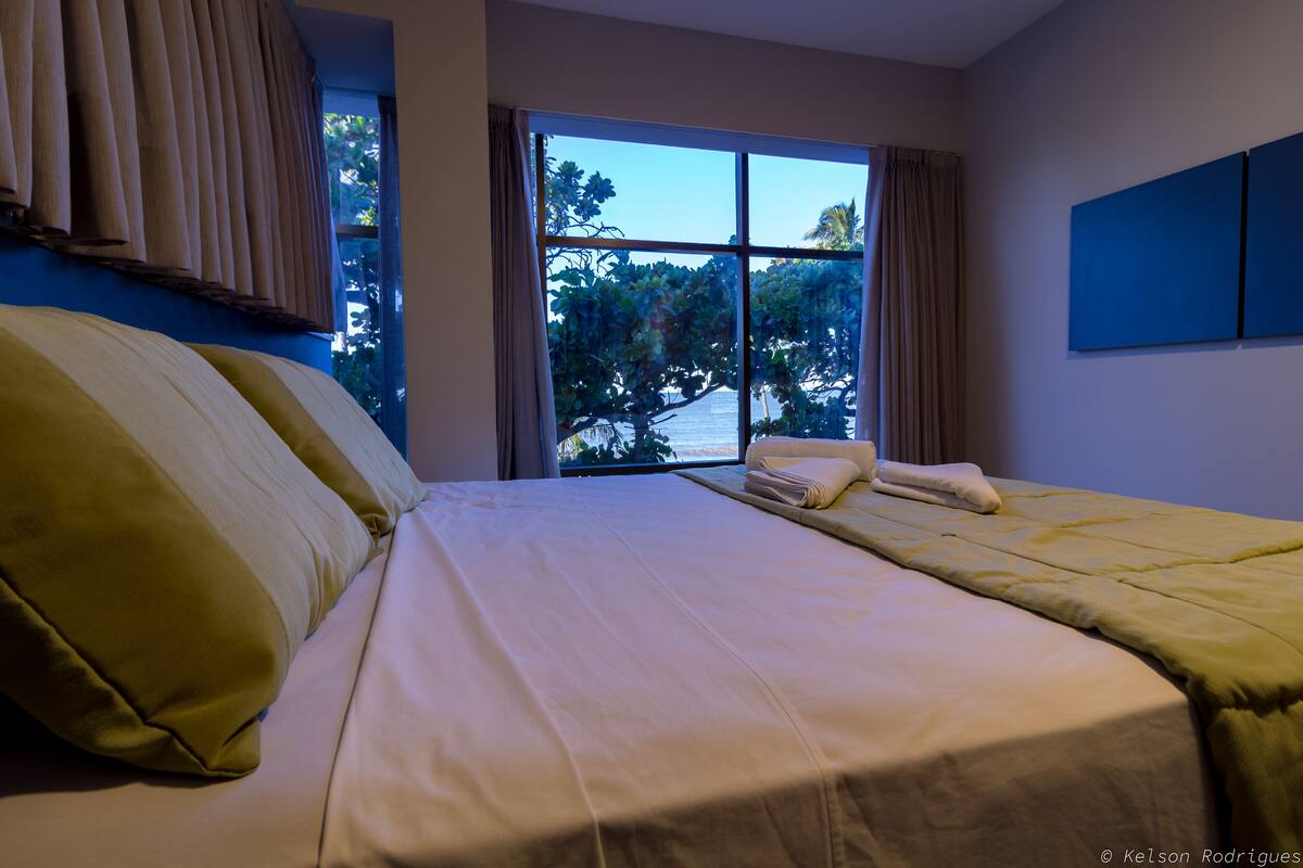 Une chambre d’hôtel avec un grand lit, une fenêtre avec des rideaux et une vue sur des arbres et un bâtiment à l’extérieur.