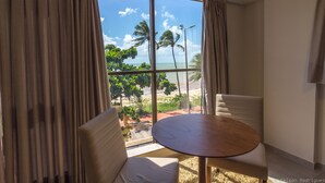A room with a large window offering a view of the beach and palm trees. There is a round wooden table and two chairs. - Hotel do Mar Cabo Branco (João Pessoa)