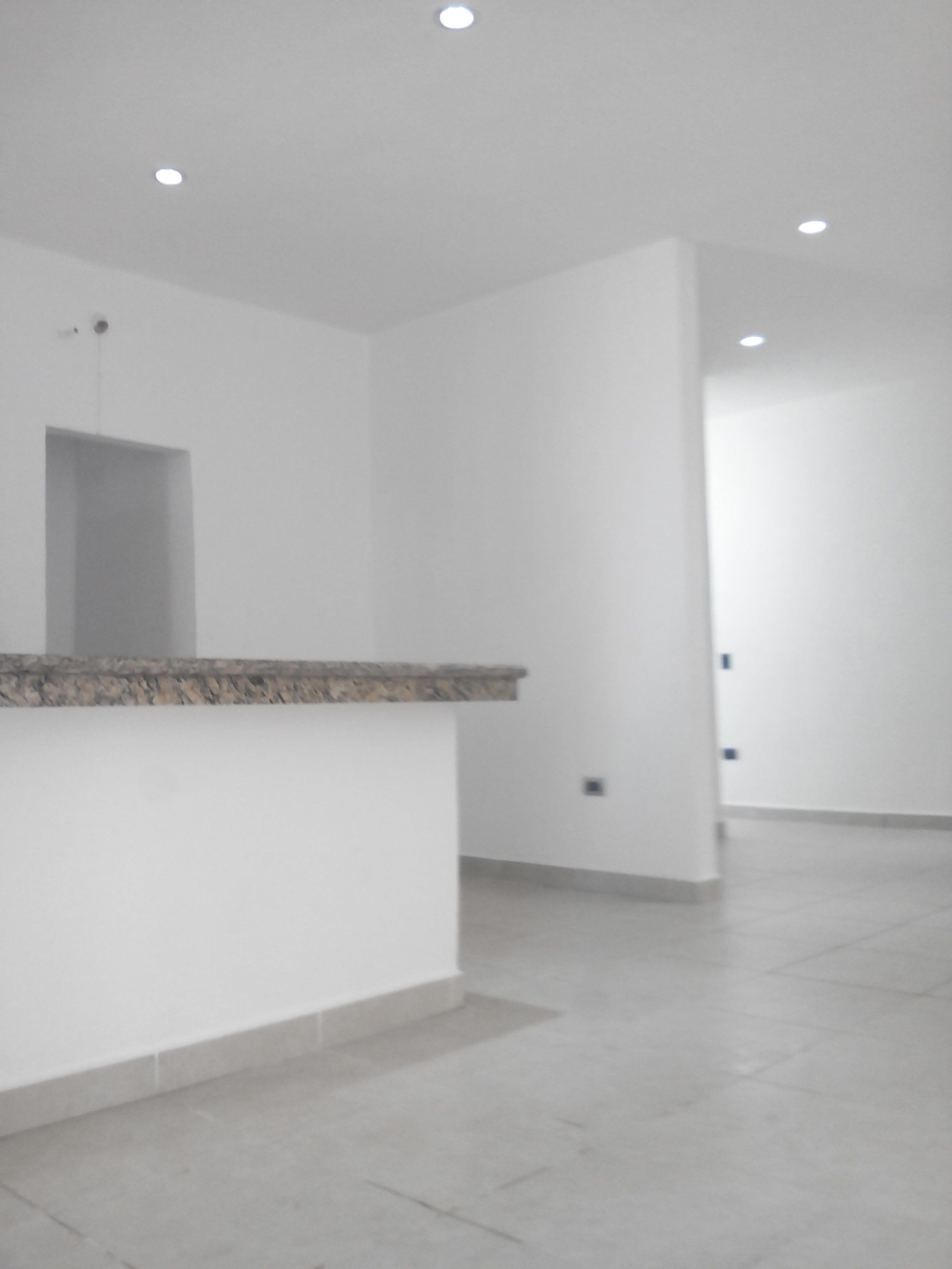 A spacious, modern interior with a minimalist design, featuring a central island counter and recessed ceiling lighting.