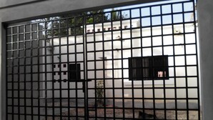 A metal fence with a grid pattern, a white building with a window, and a small tree in the background. - Casa en PlayaDelCarmen 526 by Sinbad (Playa del Carmen)
