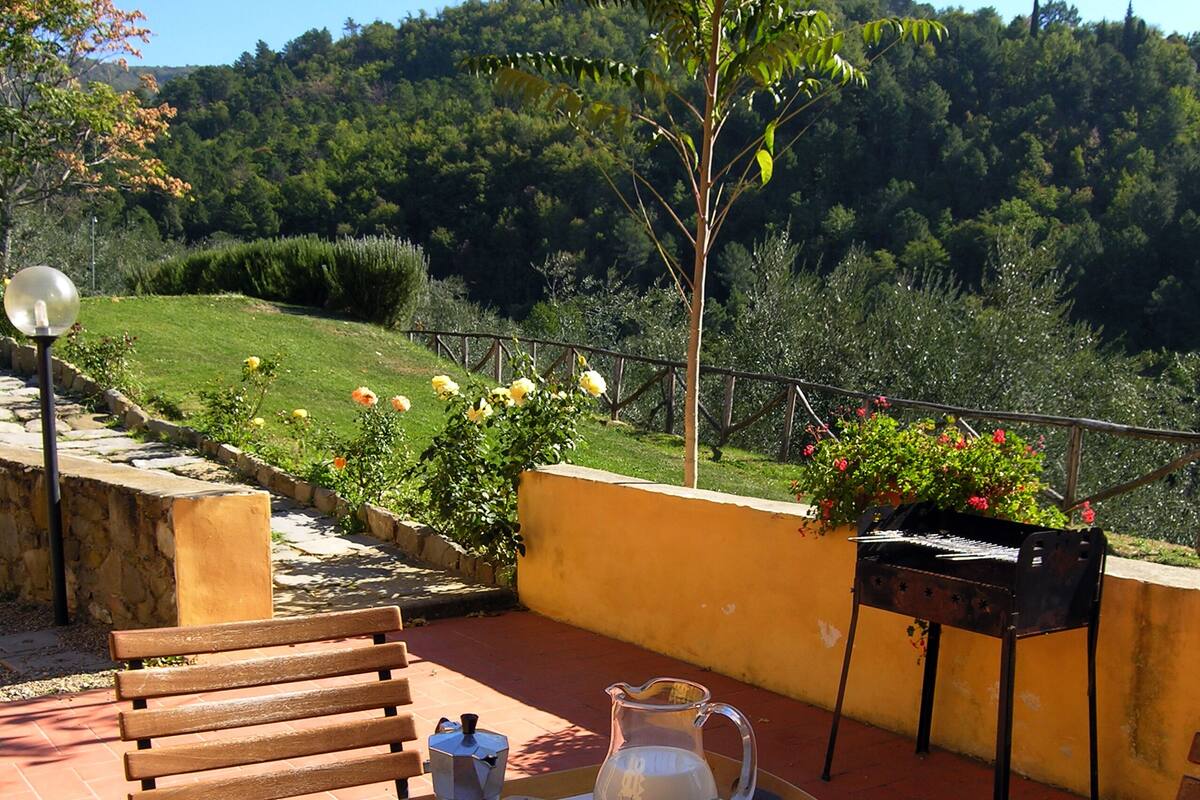 Une terrasse extérieure avec une table dressée pour le thé, entourée de verdure et offrant une vue sur une colline boisée.