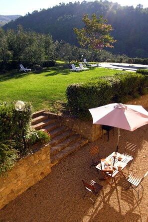 A patio with a table, chairs, and an umbrella. There are steps leading up to the patio, and a stone wall surrounds it. - Agriturismo Il Bellini (Castelfranco Piandisco)
