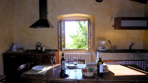 A rustic kitchen with a wooden table set for dining, a window with curtains, and a radiator. - Agriturismo Il Bellini (Castelfranco Piandisco)