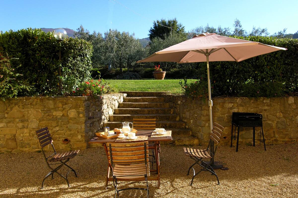 Une terrasse extérieure avec une table dressée pour deux personnes, un banc et un parasol.