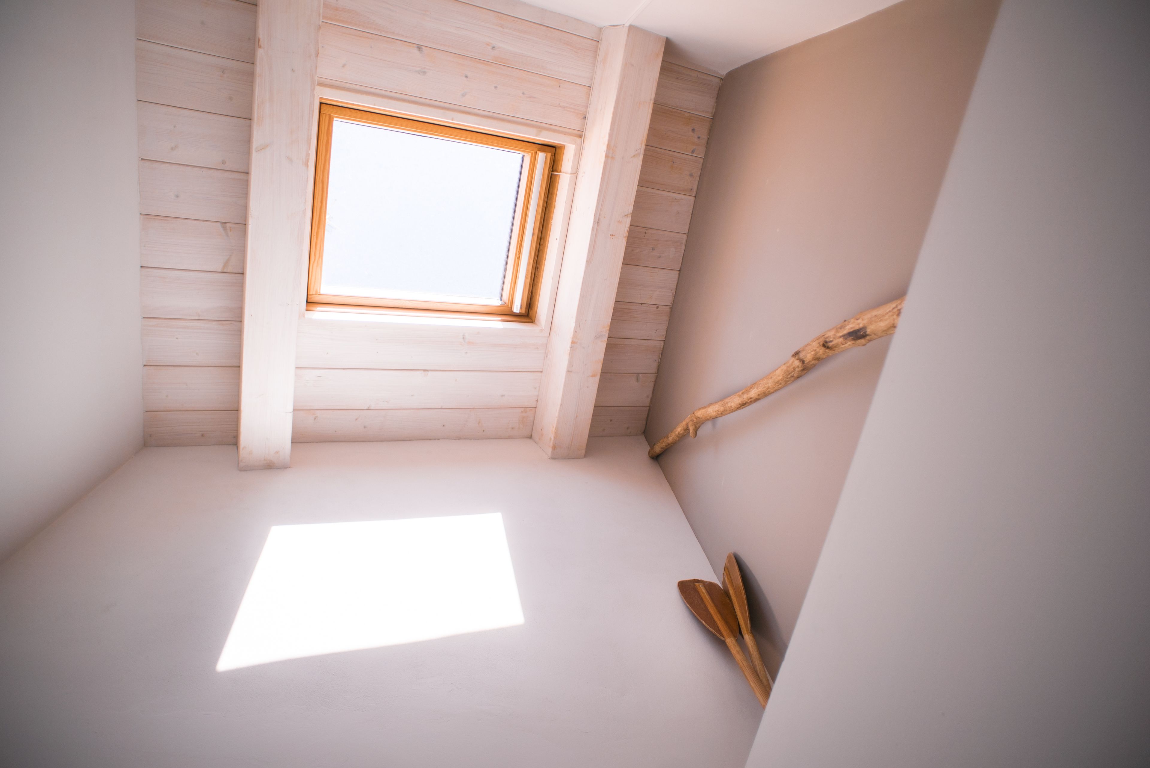 Una habitación con techo inclinado, tragaluz y viga de madera.
