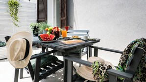 Un espacio de comedor al aire libre con una mesa preparada para dos, que incluye una variedad de frutas, un vaso de jugo de naranja y un menú.