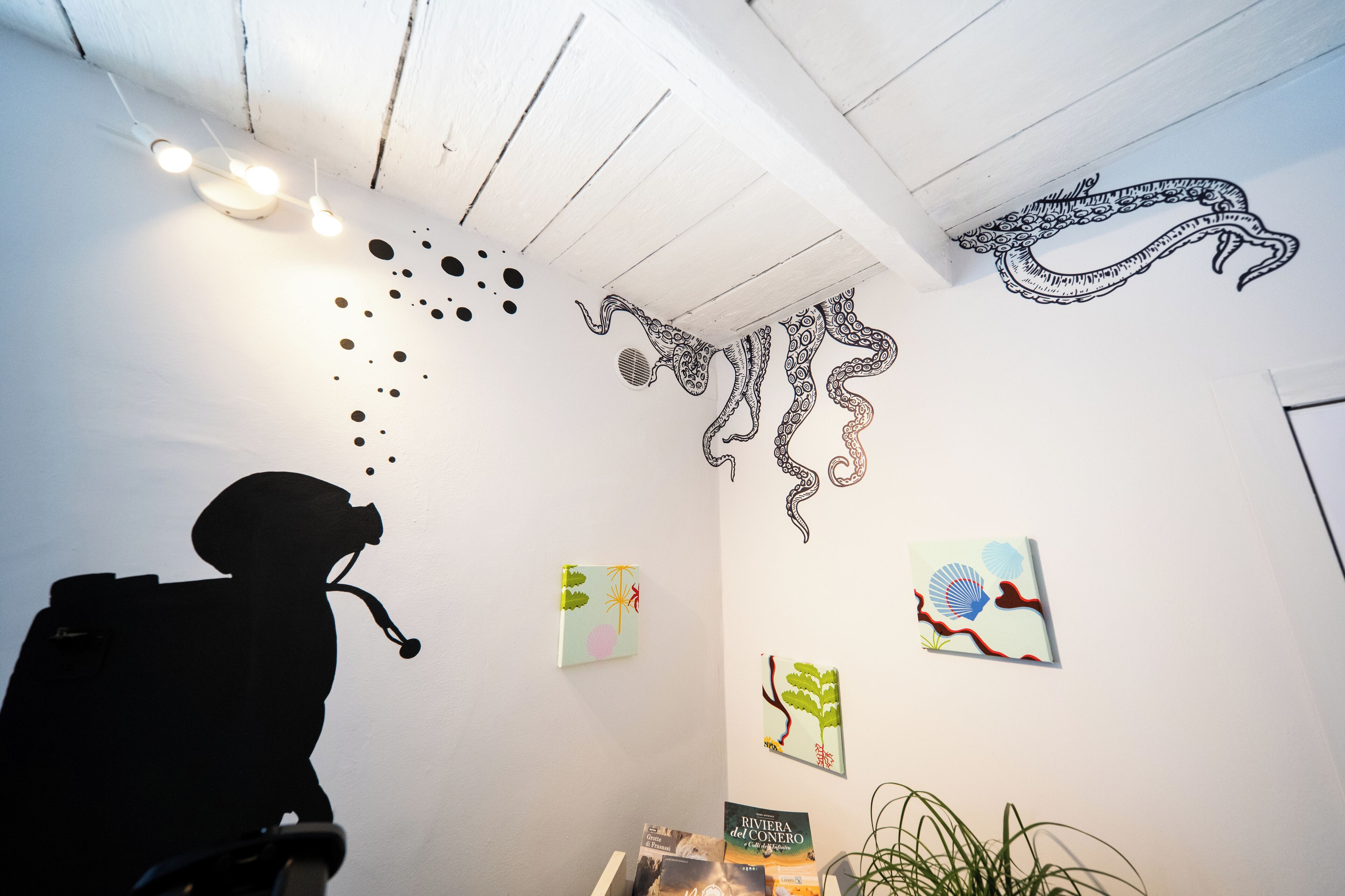A room with a white ceiling, wall art including a black octopus drawing, and a silhouette of a person.